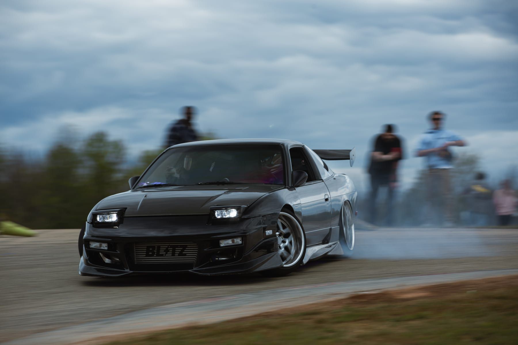 Drift car sliding past spectators under a moody sky