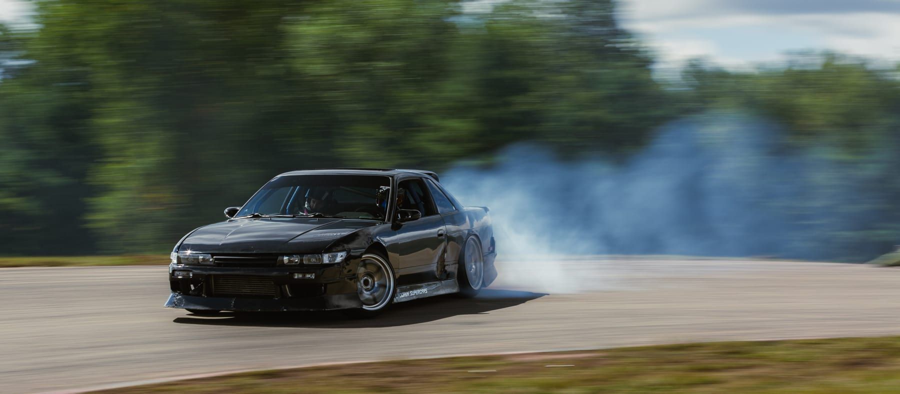 Nissan S13 drifting through a corner in a cloud of tire smoke